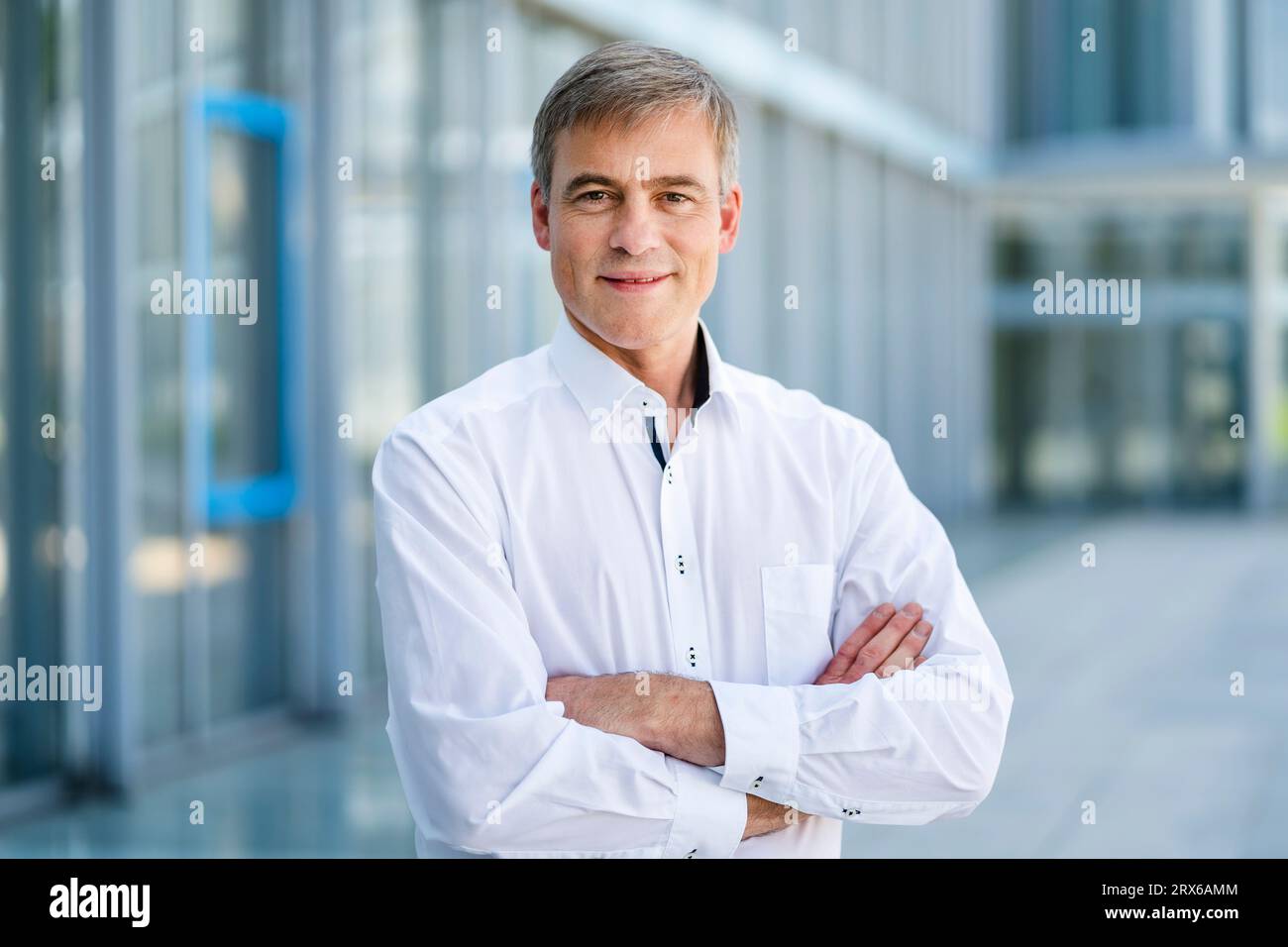 Casual businessman standing in front of office building with arms crossed Stock Photo
