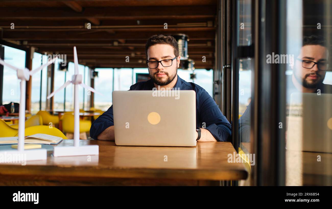 Young engineer with wind turbine models using laptop at table Stock Photo