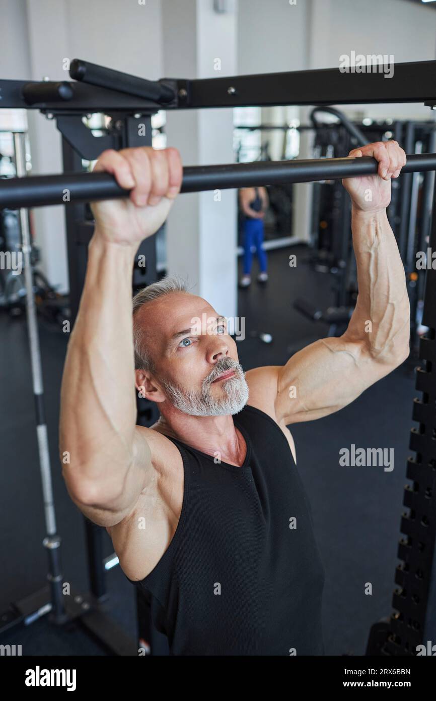 Muscular mature man doing chin-ups in gym Stock Photo