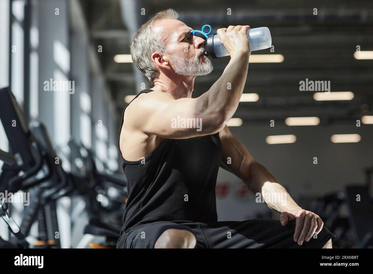Mature man drinking water in sunlight at gym Stock Photo - Alamy