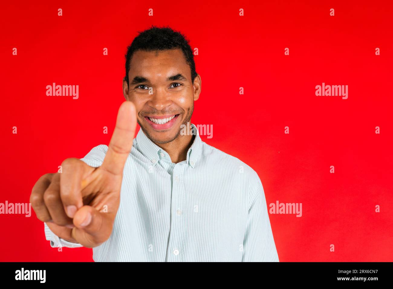 Smiling man pointing with index finger against red background Stock Photo