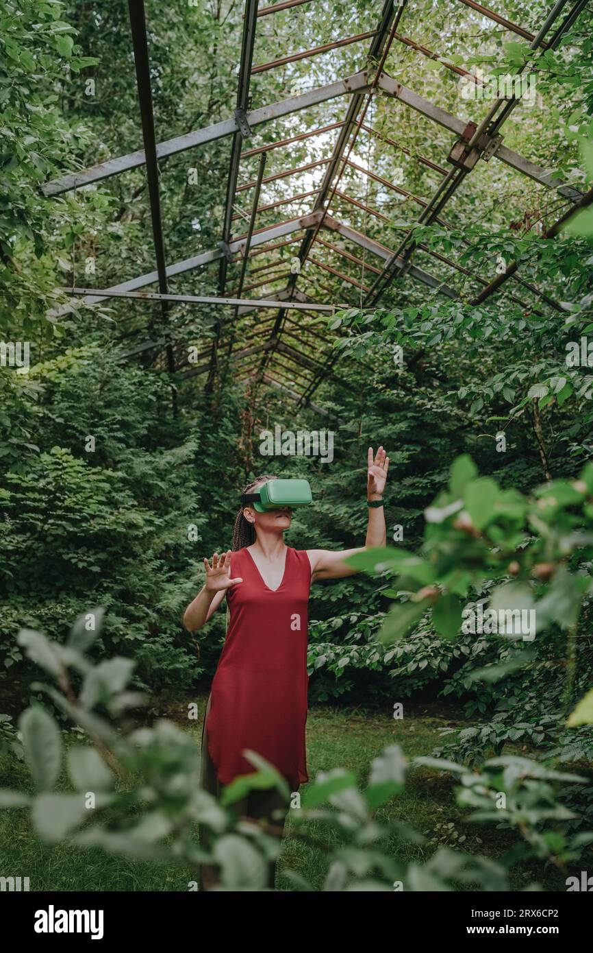 Woman wearing VR headset and gesturing in greenhouse Stock Photo