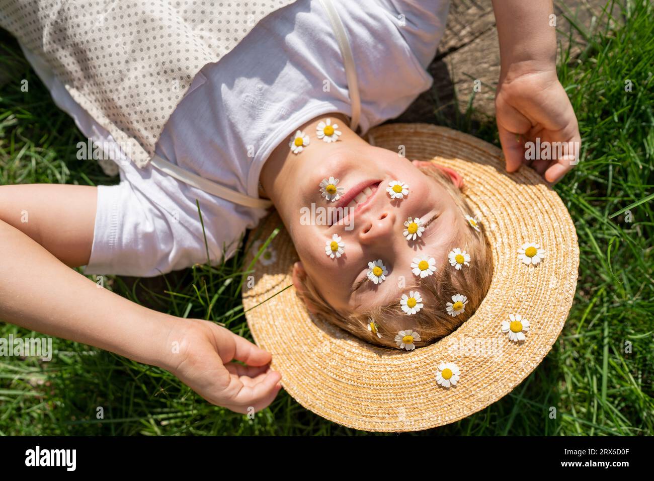 Happy boy with daisies over face relaxing on grass Stock Photo