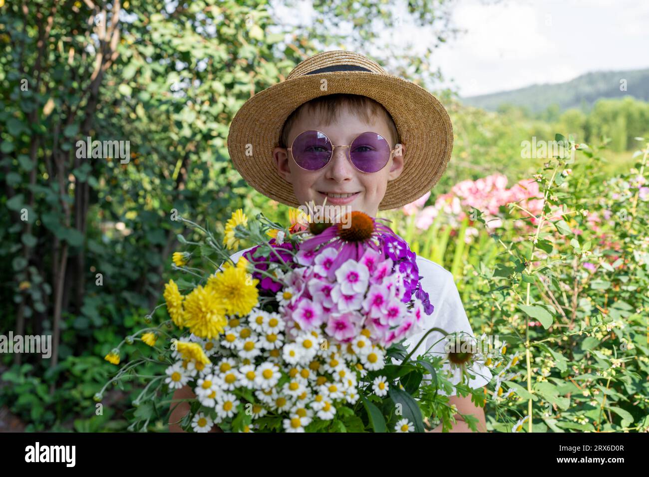 Happy boy wearing hat holding various flowers in garden Stock Photo