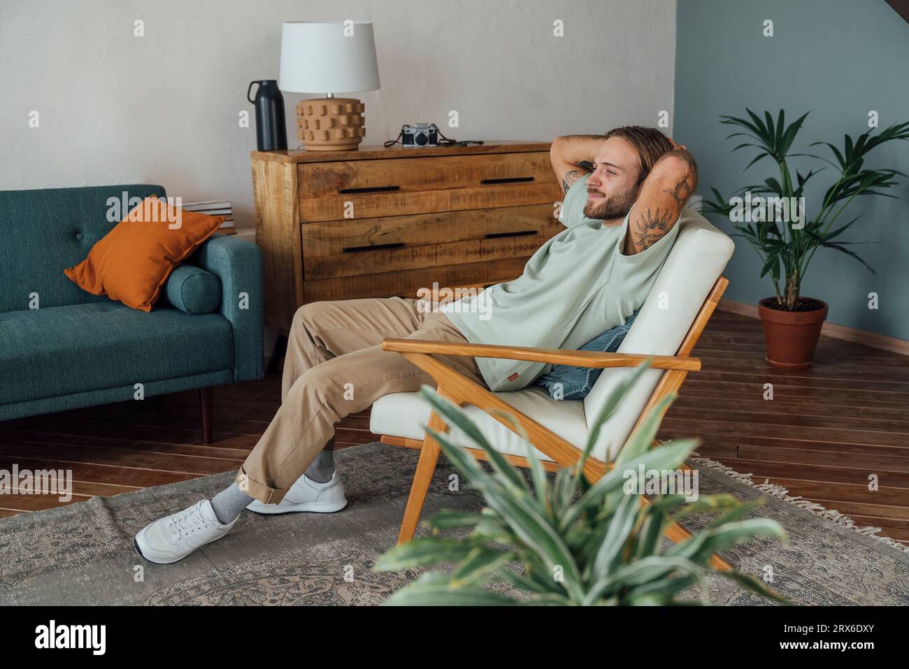 Thoughtful young man with hands behind head relaxing on armchair at home Stock Photo