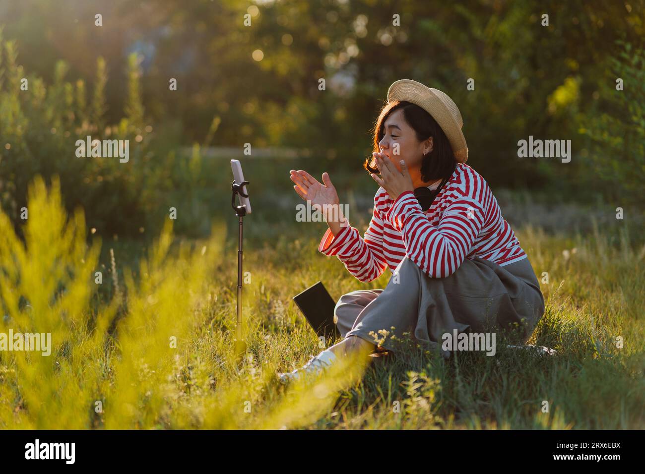 Woman blowing kiss and recording vlog on smart phone in field Stock Photo