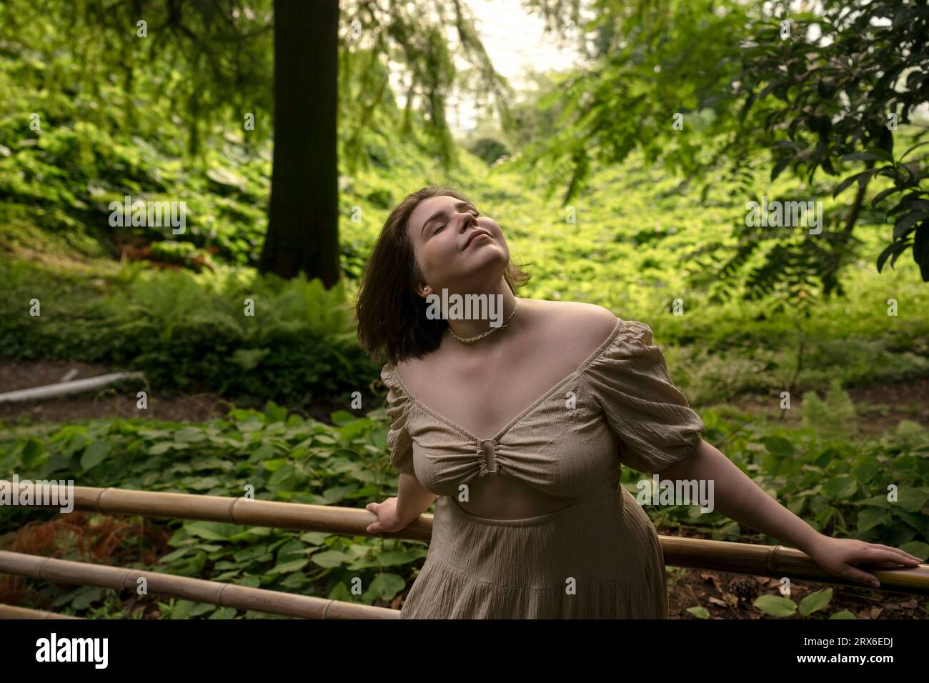 Smiling woman with eyes closed standing near fence in garden Stock Photo