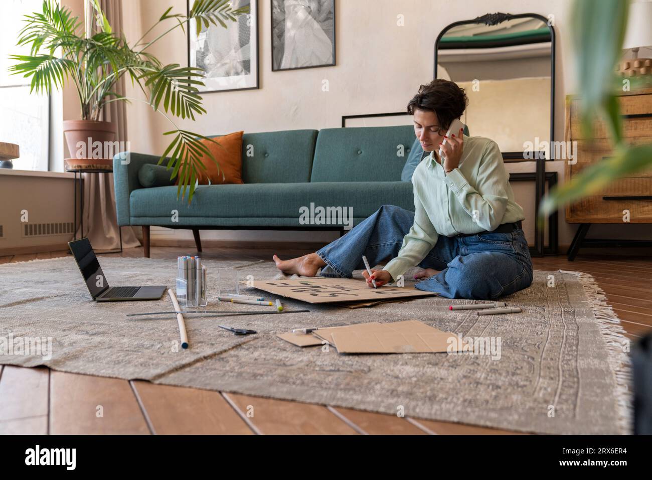 Activist making environment placard and talking on smart phone in living room at home Stock Photo