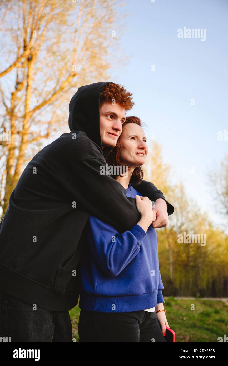 Teenage boy embracing mother in park Stock Photo