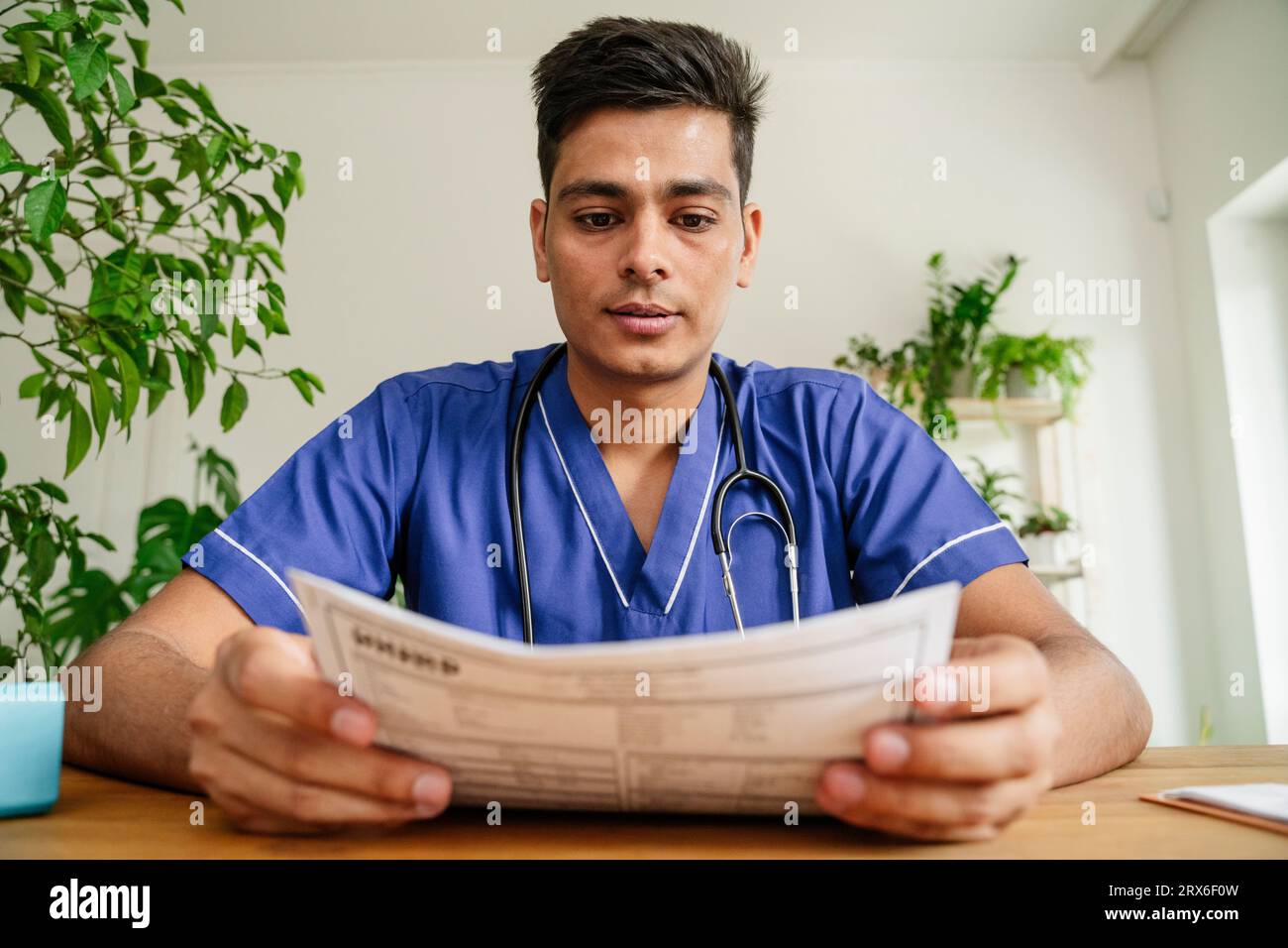 Young doctor analyzing reports at desk in clinic Stock Photo