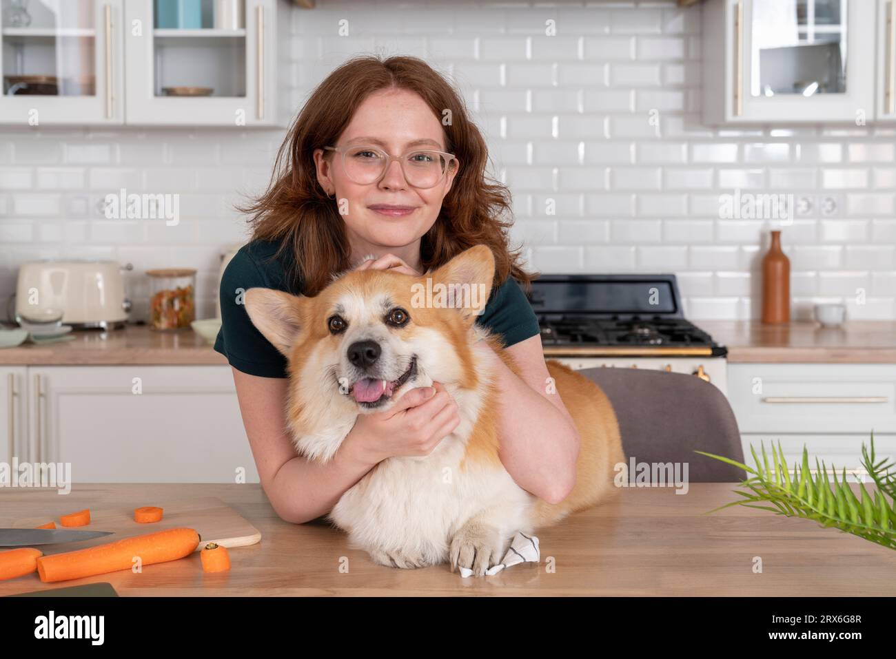 Smiling woman with Welsh Corgi dog in kitchen Stock Photo