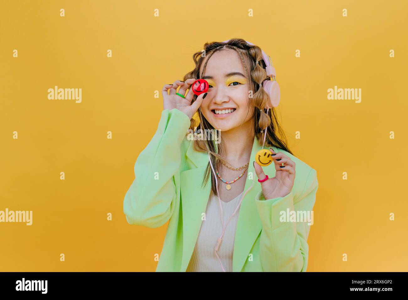 Smiling woman with headphones holding smileys against yellow background Stock Photo