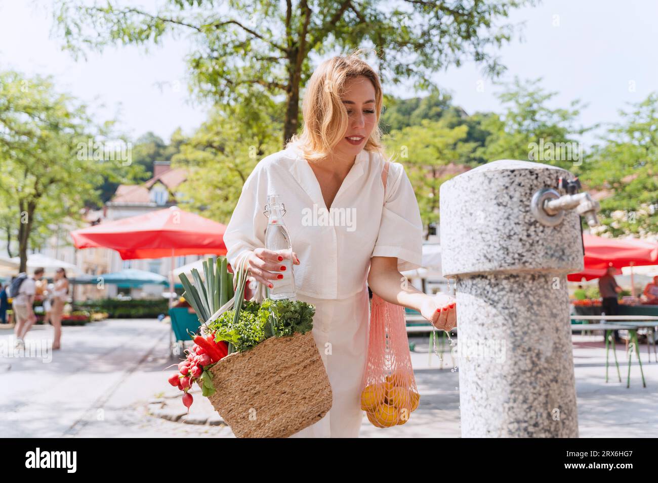 Woman with bags of groceries fetching water from drinking fountain Stock Photo