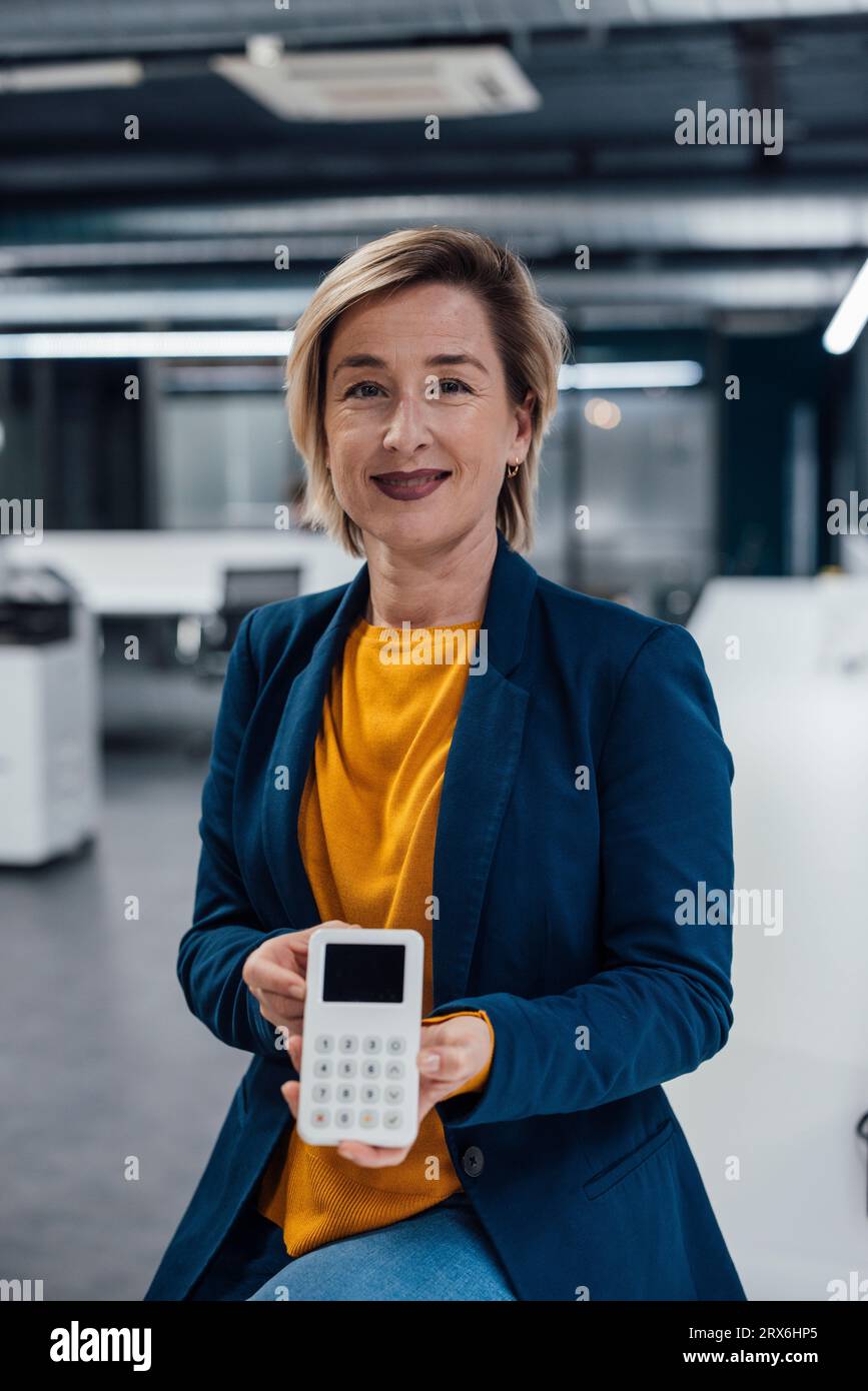 Smiling businesswoman holding modern POS terminal in office Stock Photo
