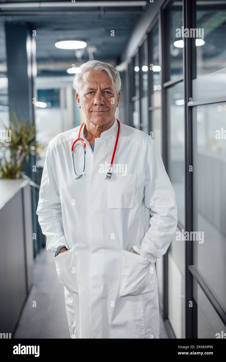 Confident senior doctor with hands in pockets at hospital Stock Photo