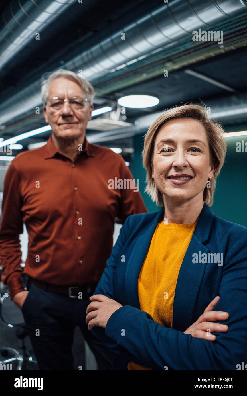 Smiling businesswoman with arms crossed by colleague in office Stock Photo
