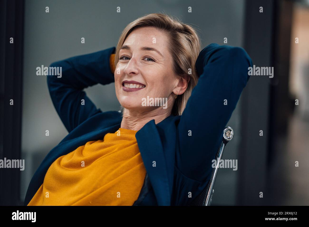 Smiling businesswoman with hands behind head at work place Stock Photo