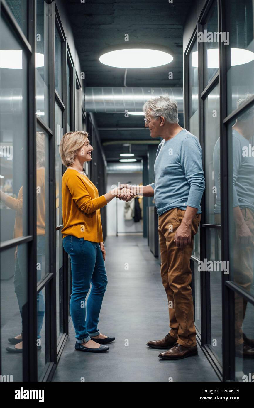 Business colleagues doing handshake in corridor at work place Stock Photo
