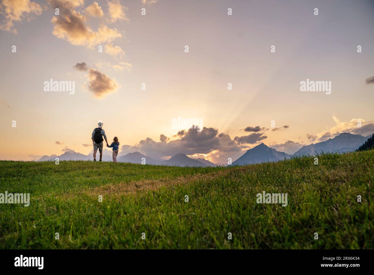 Father and daughter exploring in meadow by mountain range Stock Photo
