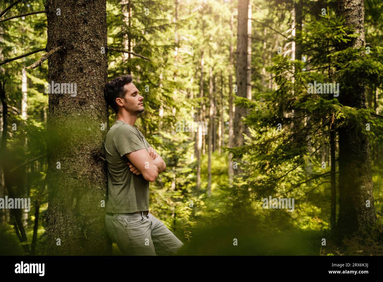 Hiker with arms crossed leaning on tree at forest Stock Photo