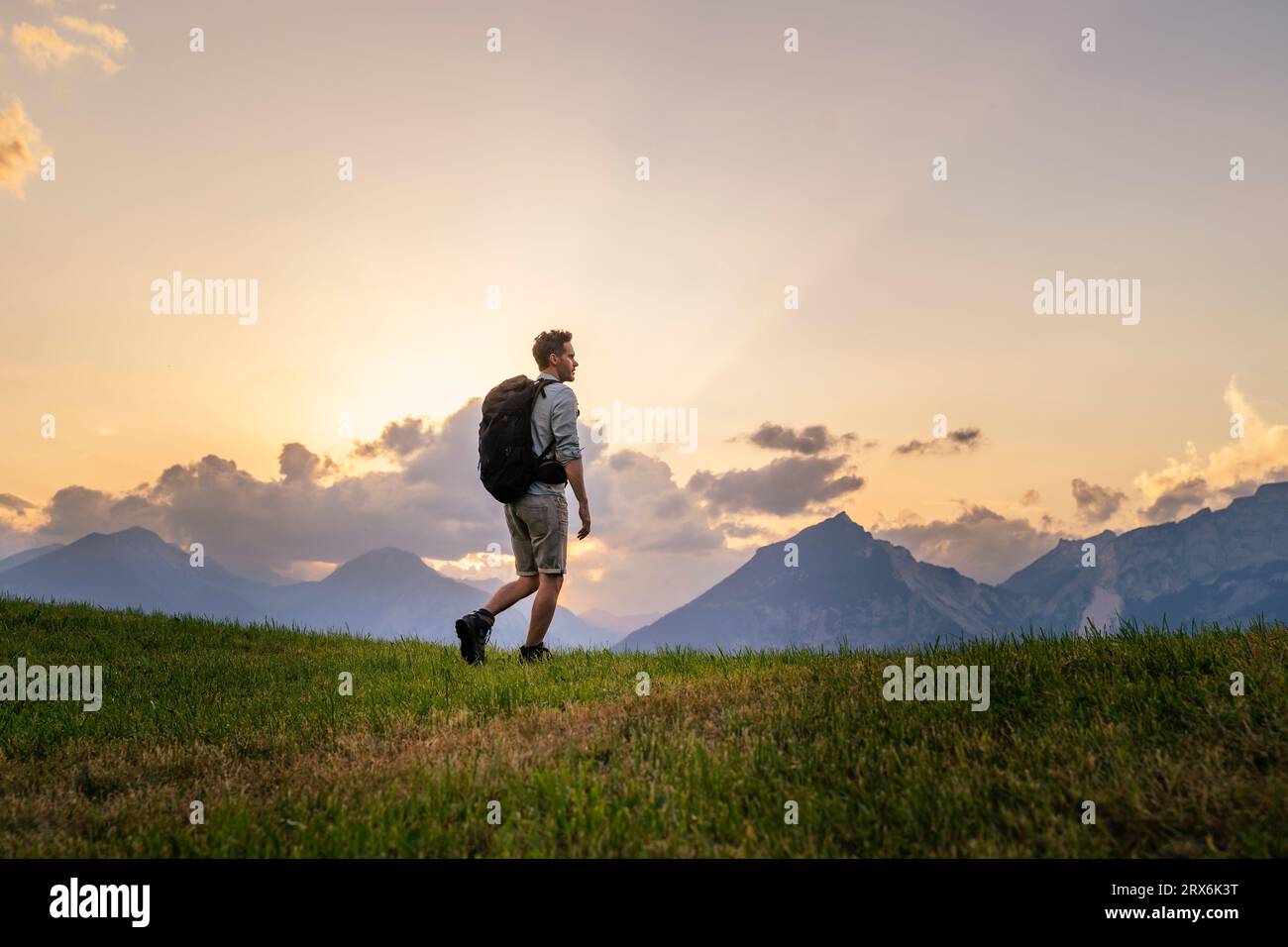 Hiker with backpack exploring in meadow at sunset Stock Photo