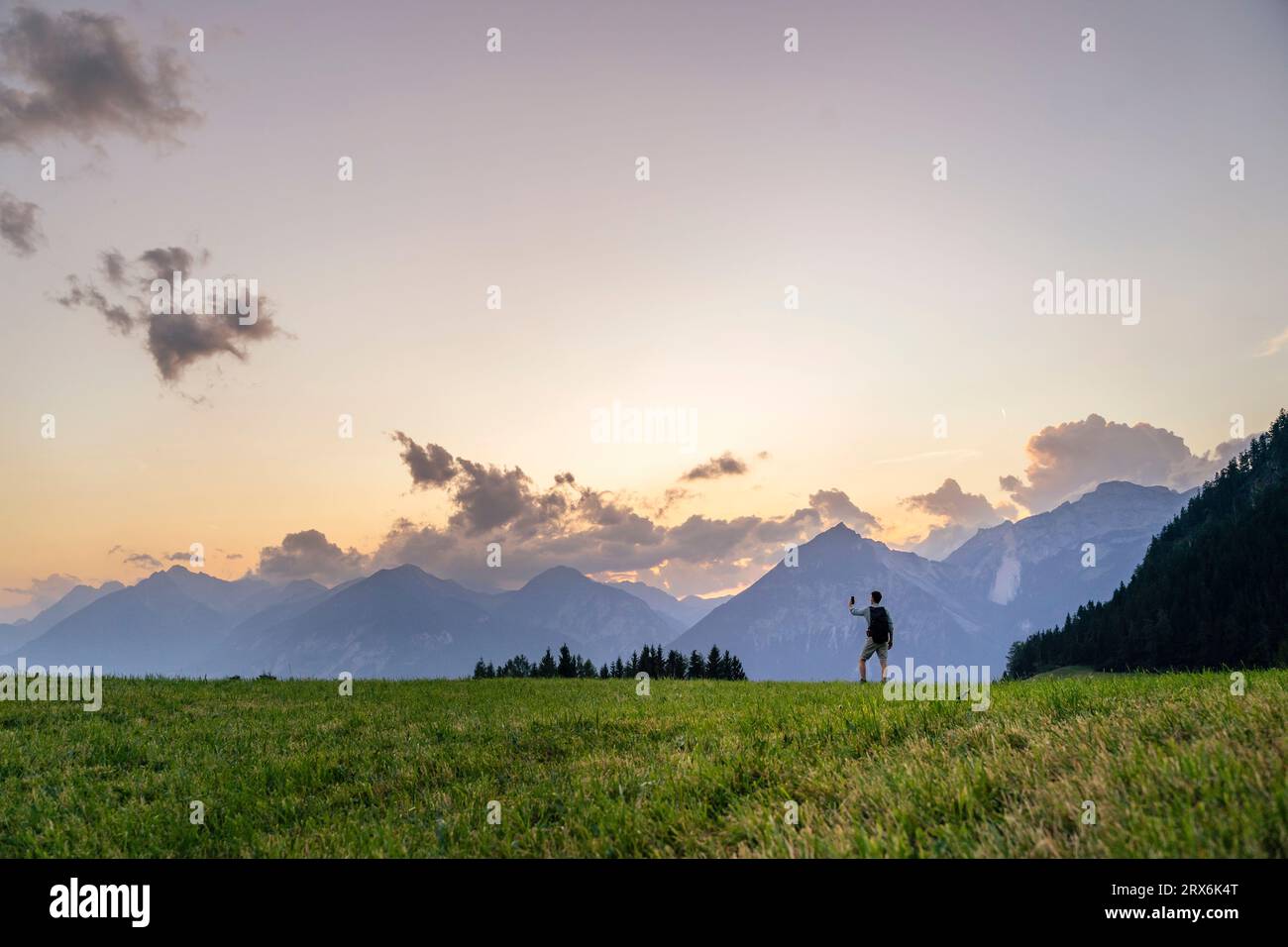 Man hiking in meadow by mountain range Stock Photo