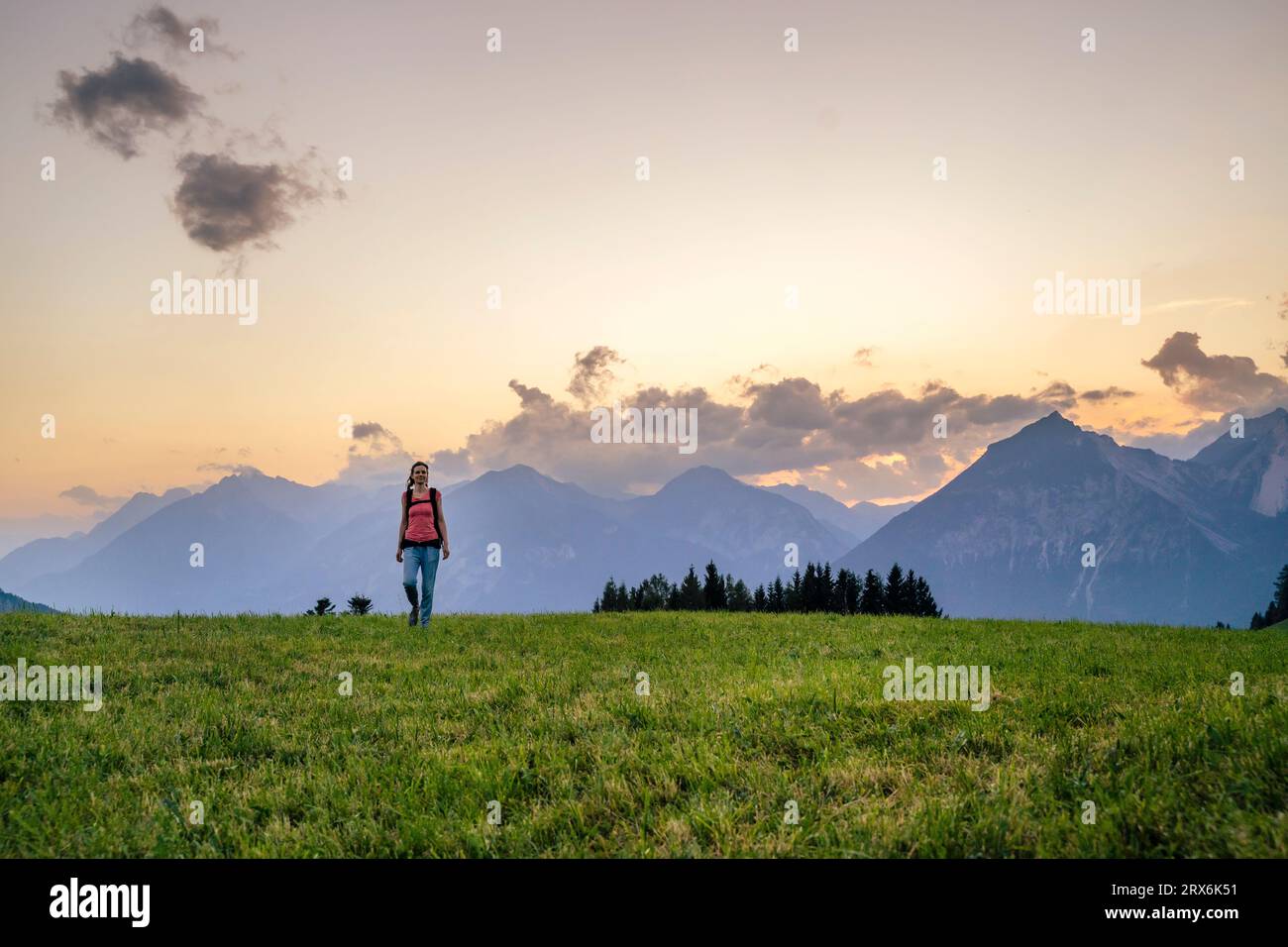 Woman hiking in meadow at sunset Stock Photo
