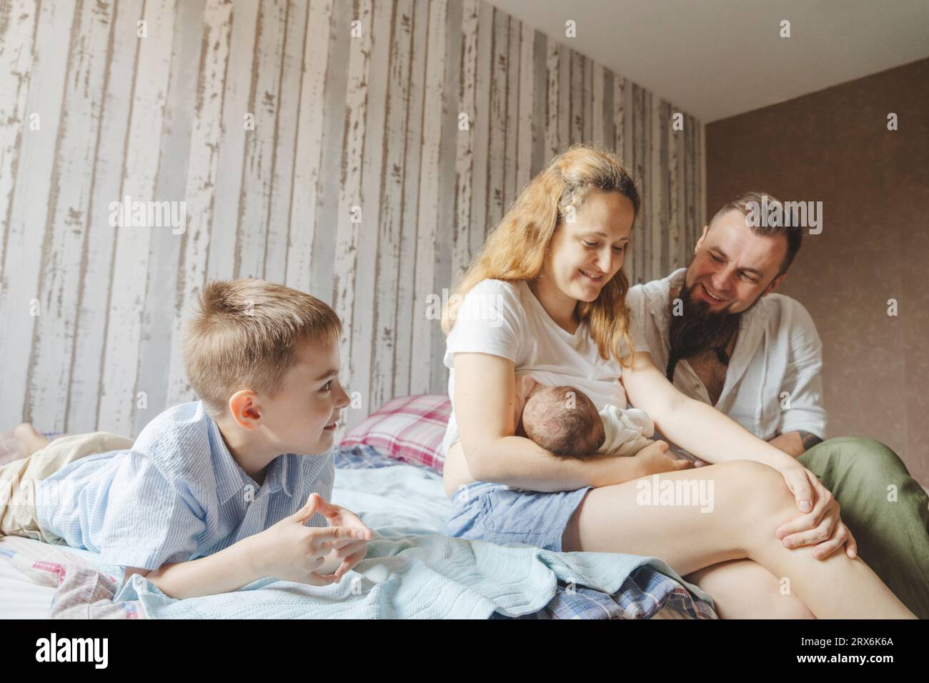 Happy mother breastfeeding newborn daughter on bed at home Stock Photo