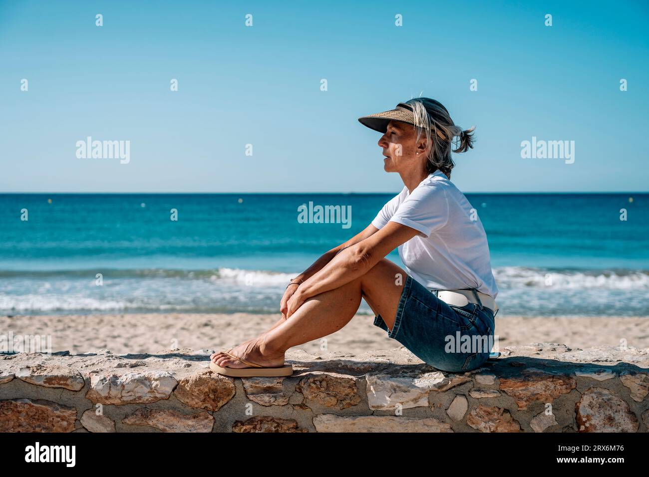 Side view of woman sitting on wall by the beach hi-res stock ...