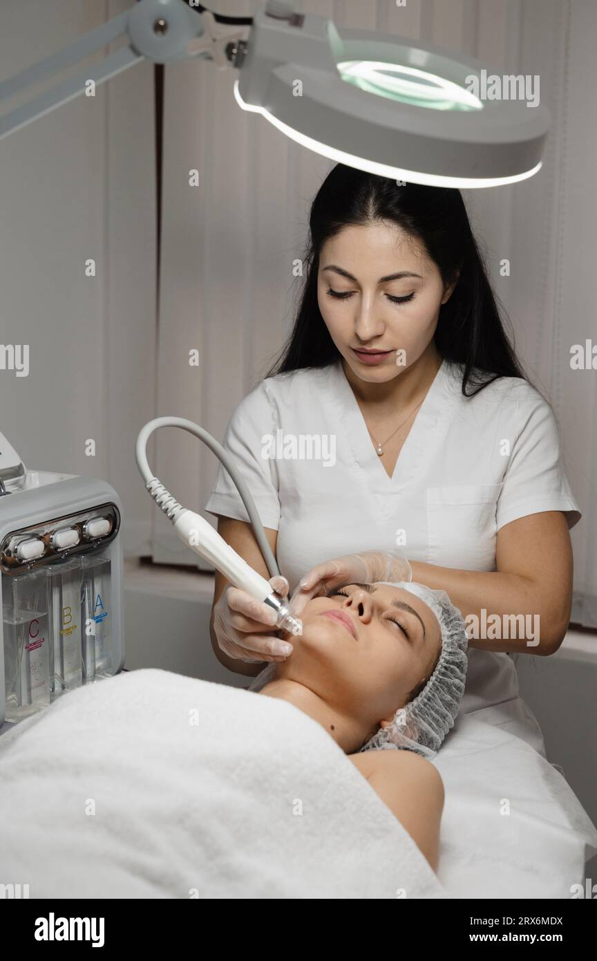 Young dermatologist proceeding microdermabrasion treatment on woman