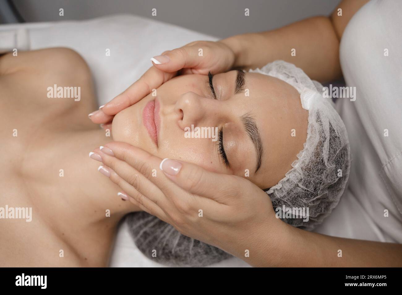 Beautician giving facial massage to young woman with hands Stock Photo