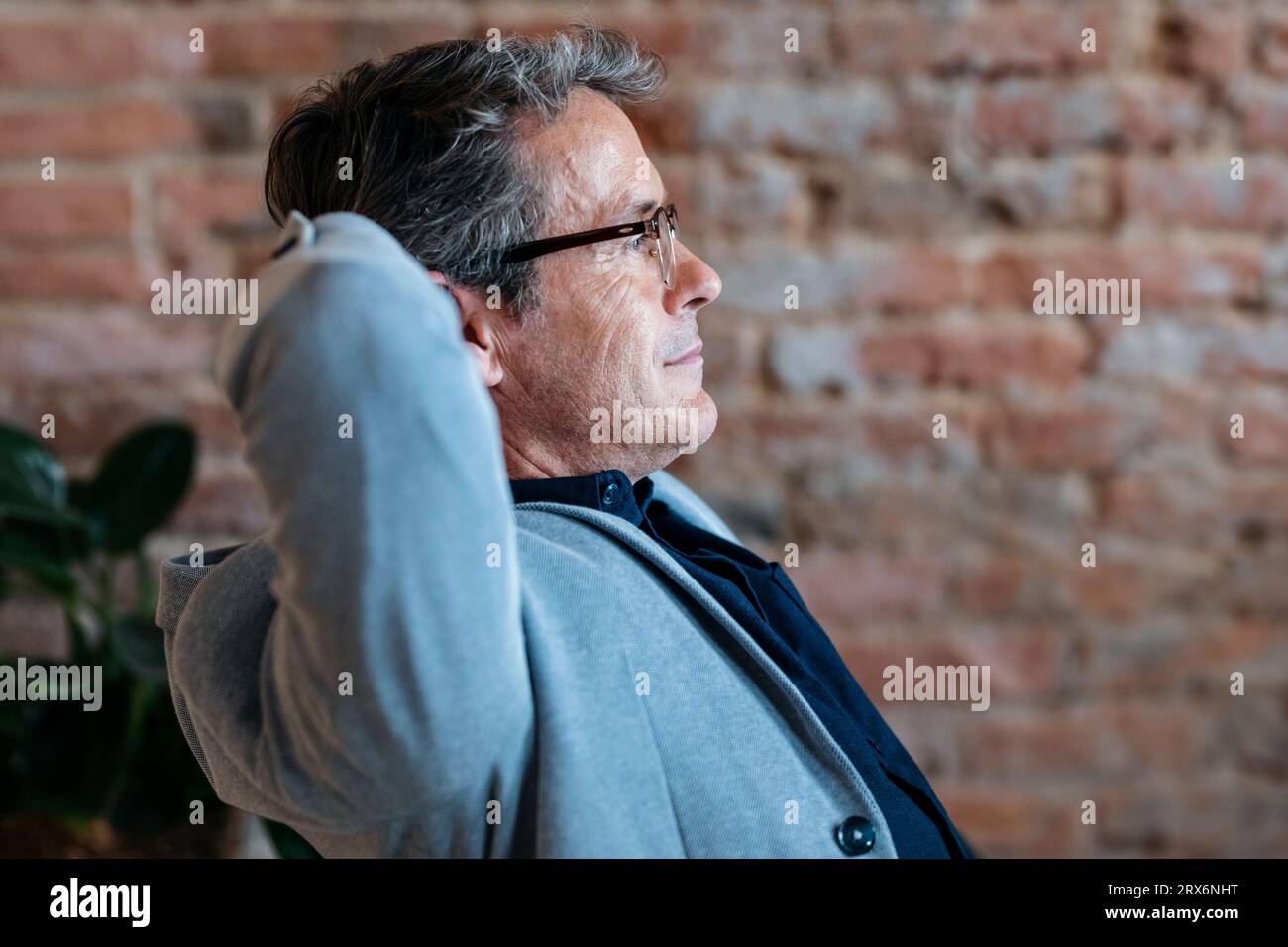 Thoughtful businessman with hands behind head in front of brick wall Stock Photo