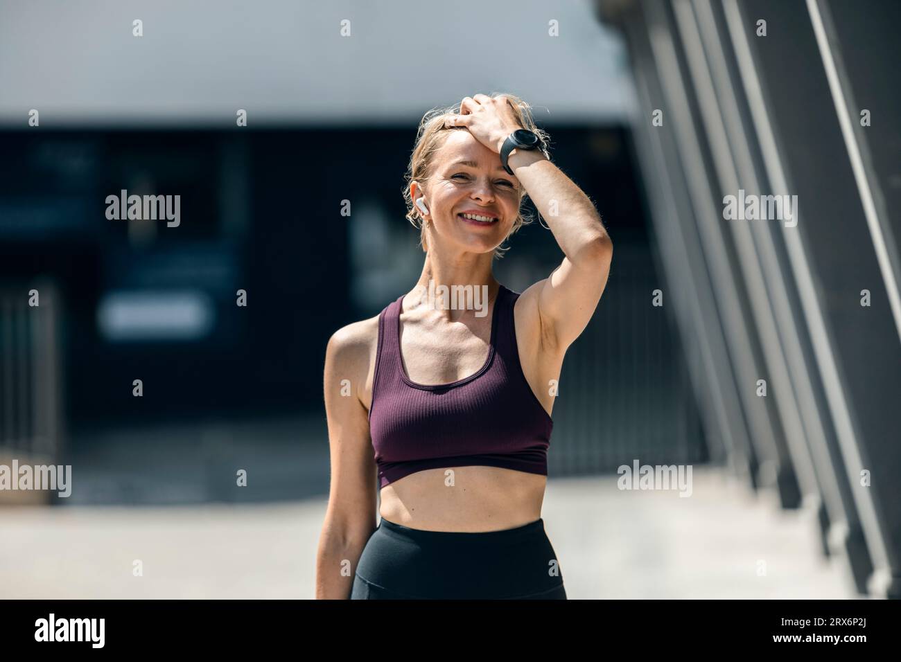 Smiling woman wearing wireless in-ear headphones standing near building Stock Photo