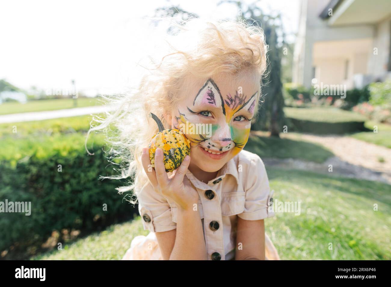 Happy girl with face painting holding small pumpkin on sunny day Stock Photo