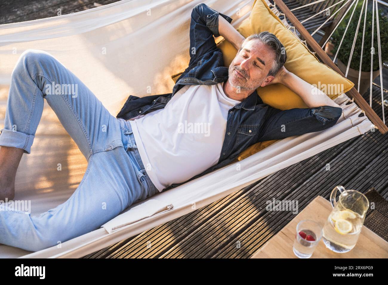 Tired man with hands behind head sleeping in hammock Stock Photo