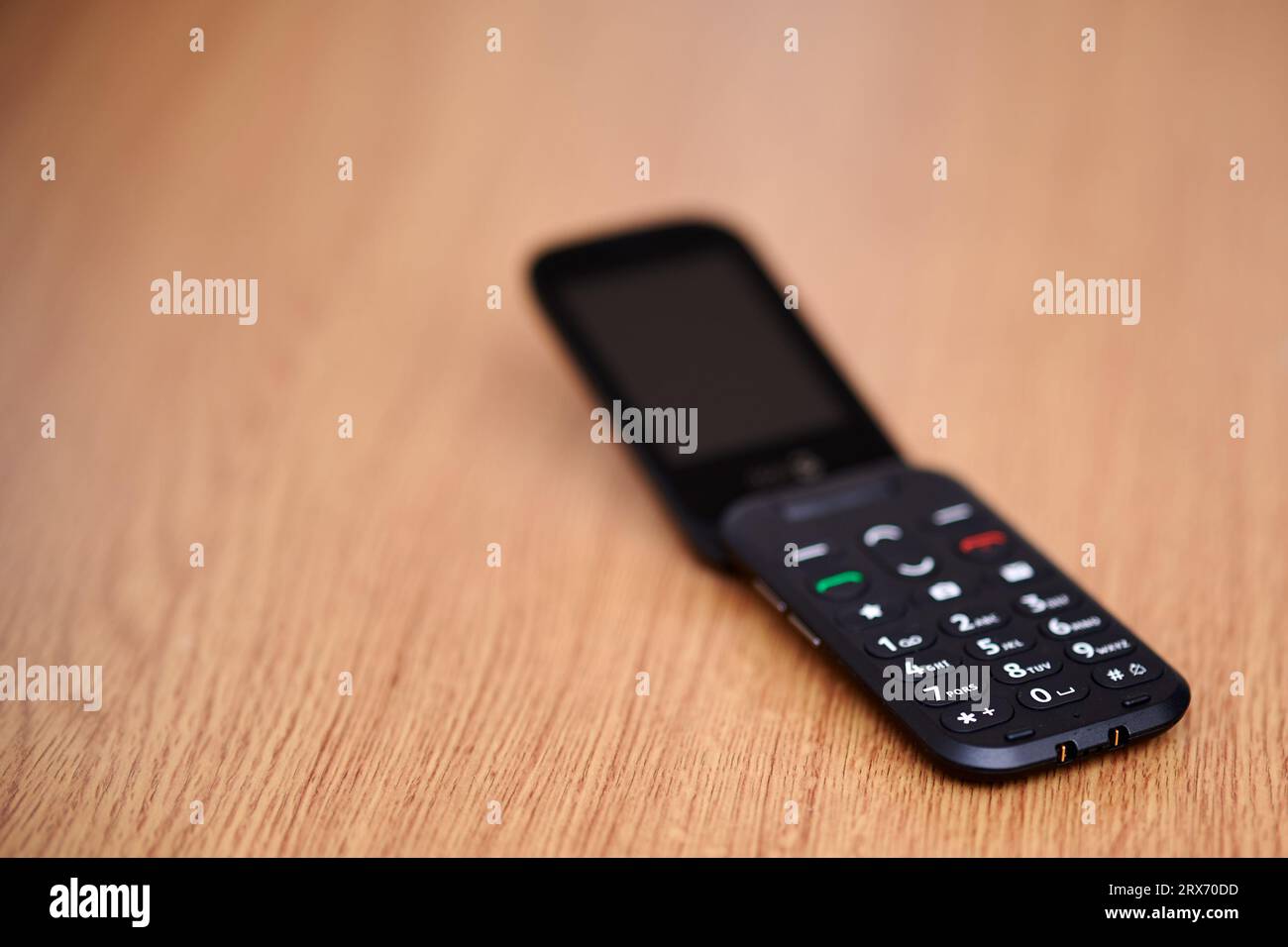 16 Sep 2023 - England  UK : Old style dumb mobile phone clam phone on wooden table Stock Photo