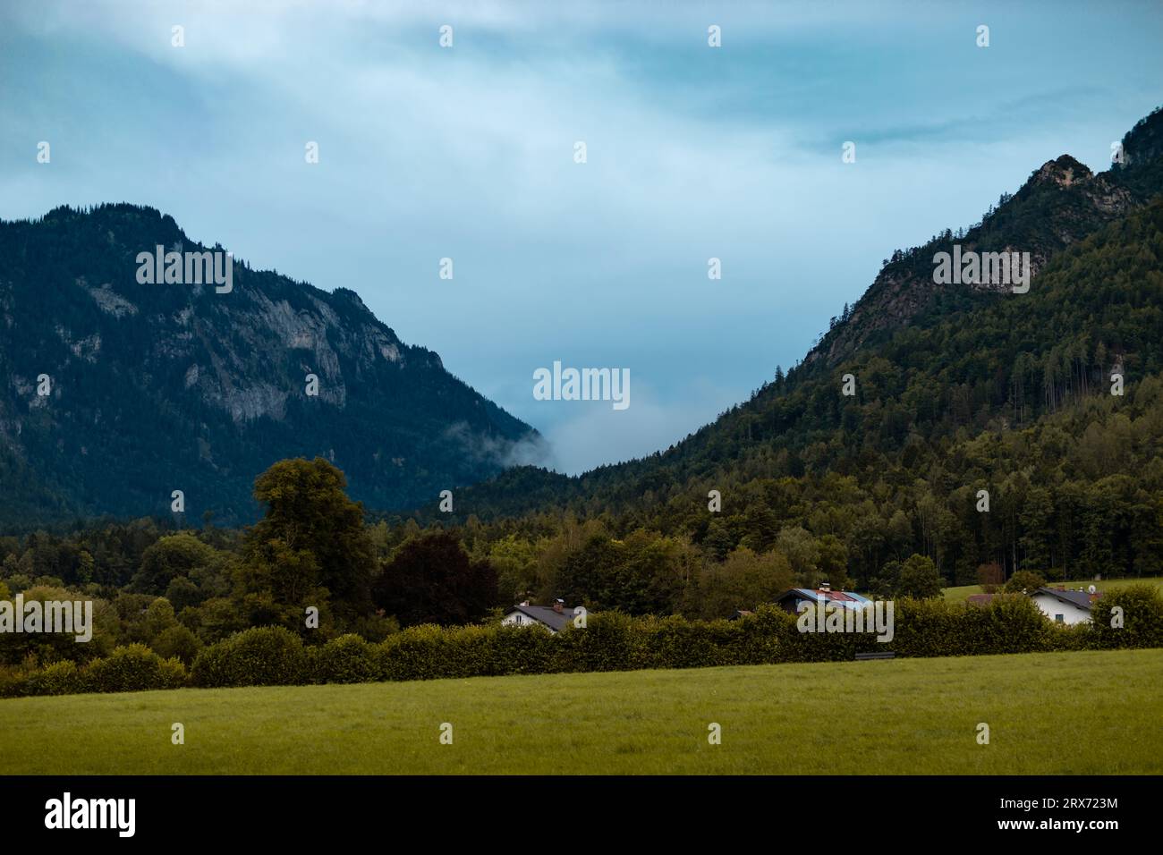 Misty clouds in between the mountains moving into the valley. Rainy weather at the German Alps region. Water vapor from the forest is in the air. Stock Photo