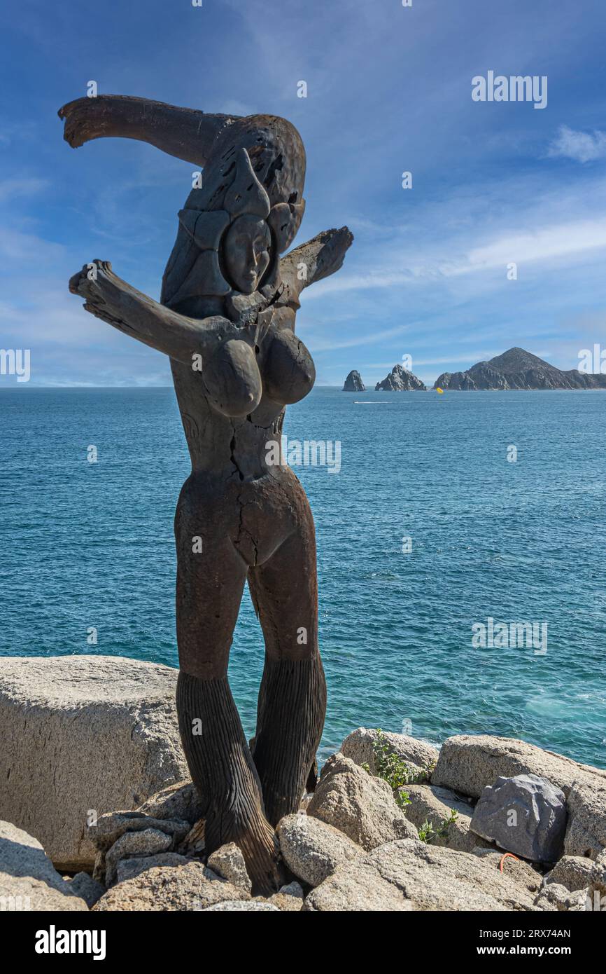 Mexico, Cabo San Lucas - July 16, 2023: Driftwood Monalisa statue on cliffs above Playa del Rey with Reserva de lobos Marinos on horizon behind blue o Stock Photo