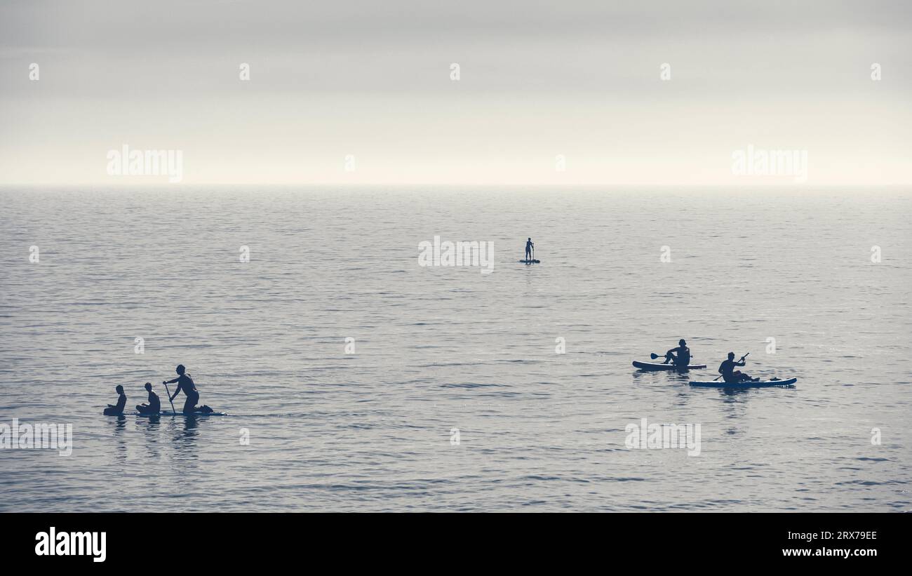 black and white image of people paddleboarding off the coast of Worthing, West Sussex, UK Stock Photo