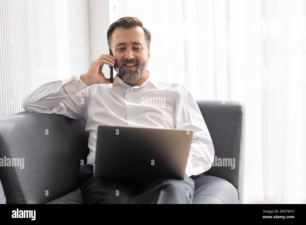 Happy senior manager business man relax at office sofa calling with friend while using laptop comfortable success people lifestyle Stock Photo