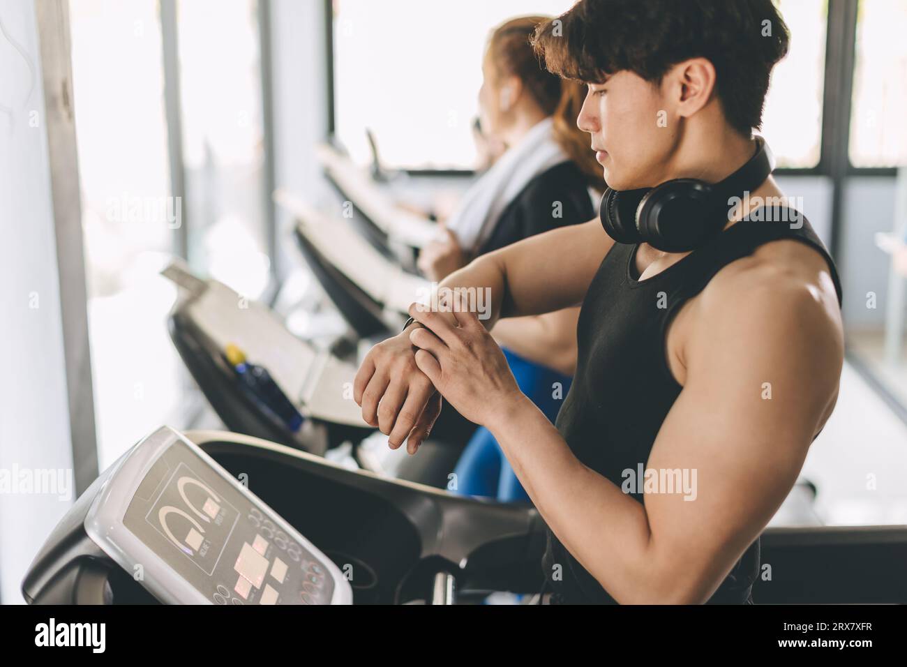 People running on a treadmill in health club using Smart Watch tracking pulse and training time for health goal Stock Photo