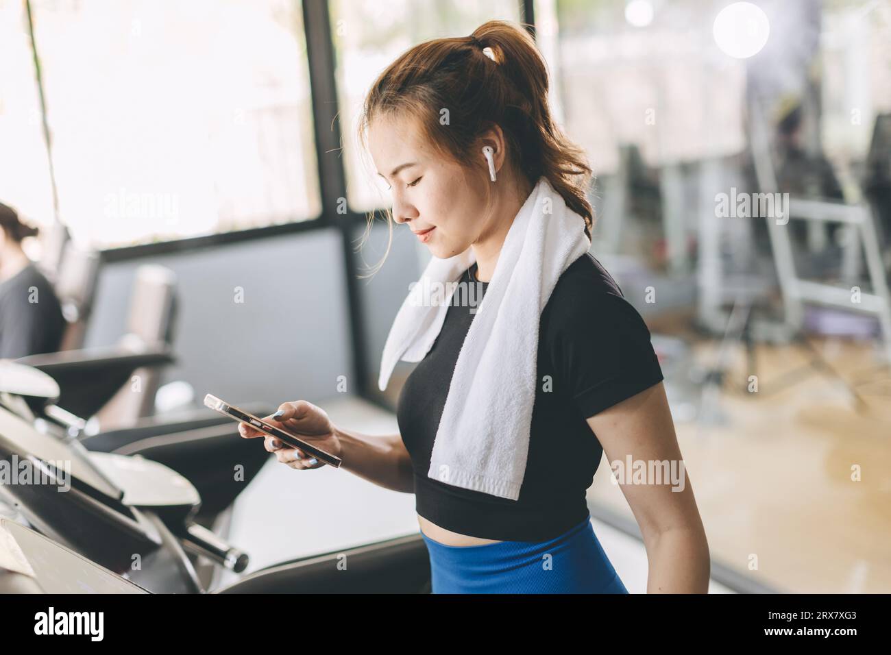 Sport woman on a treadmill using Smartphone checking Email reading news listening music or looking information from health tracking app. Stock Photo