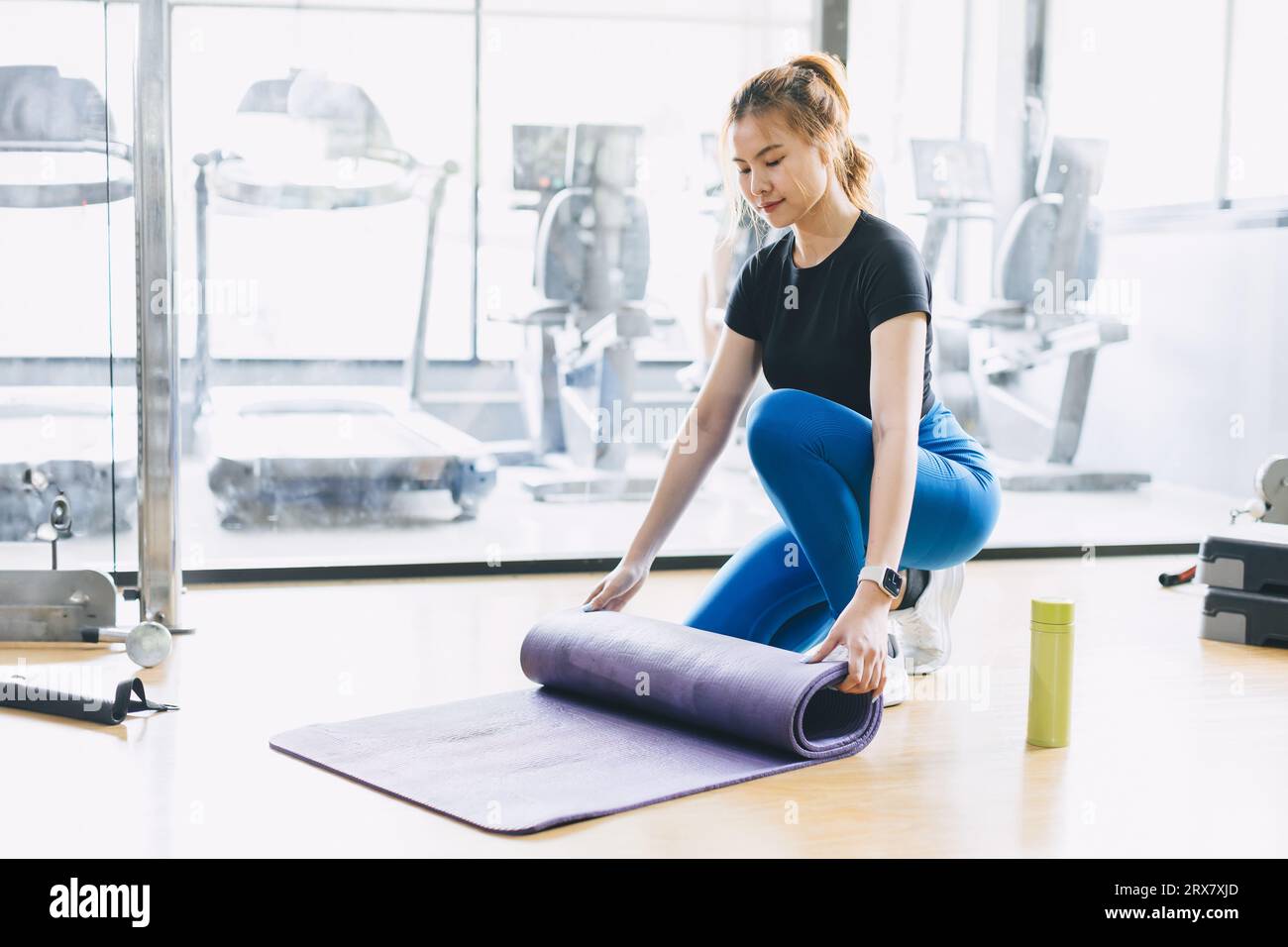 Fitness woman in sport club studio with yoga mat. Young woman roll pilates mat at a fitness training class. Stock Photo