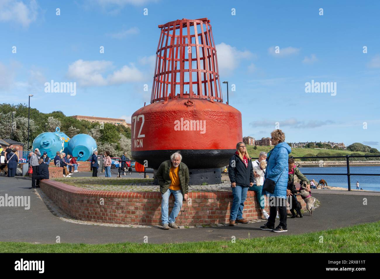 People sit at the giant red buoy marking the location of the National Cycle Network Route NCN or Hadrian's Cycleway, for cyclists. North Shields, UK Stock Photo