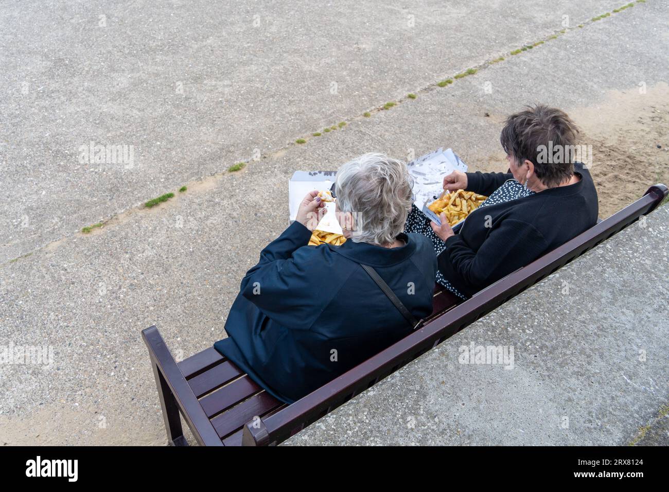 Two people sitting on a bench outdoors, seen from above, have fish and chips for Friday lunch on the Fish Quay, North Shields, North Tyneside, UK Stock Photo