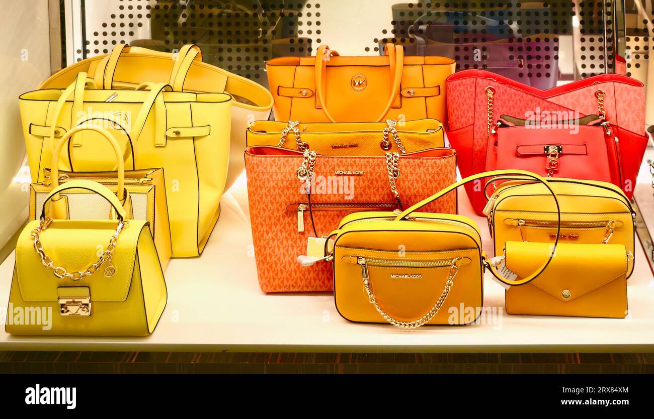 Shelf display of orange yellow and red handbags on sale in Michael Kors outlet shop at Ashford Design Outlet Ashford Kent England UK Stock Photo
