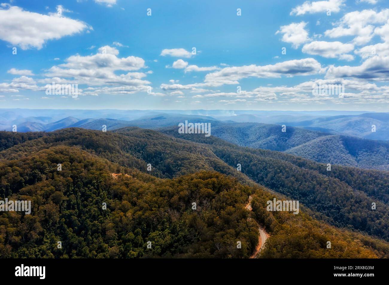 Thunderbolts way through woods covered great dividing range mountain ranges in Australia with distant bushfire in aerial landscape. Stock Photo