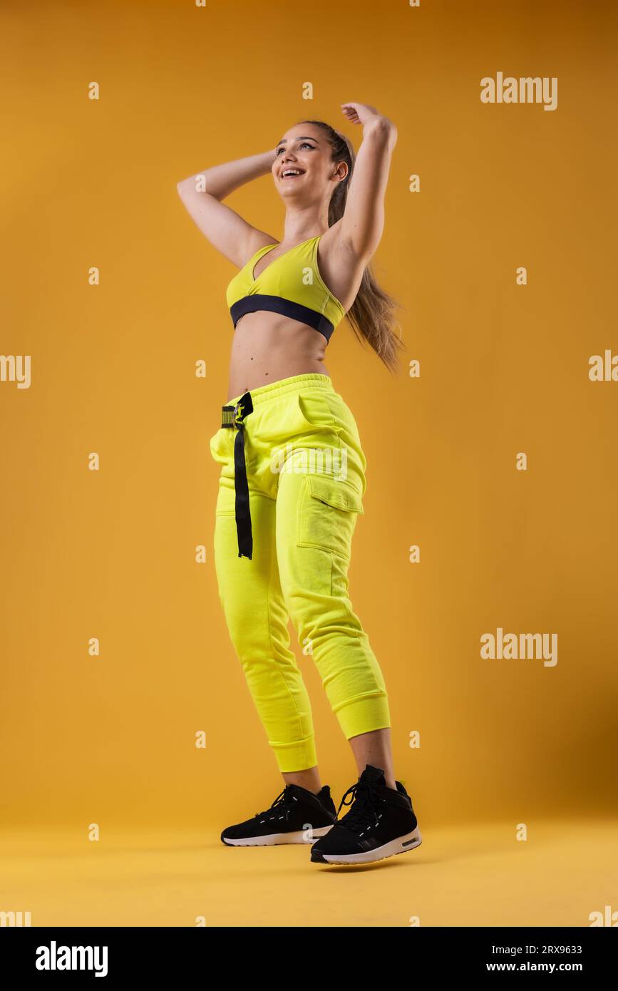 beautiful girl in yellow outfit dancing zumba happy dance instructor against dark yellow or orange background 2RX9633