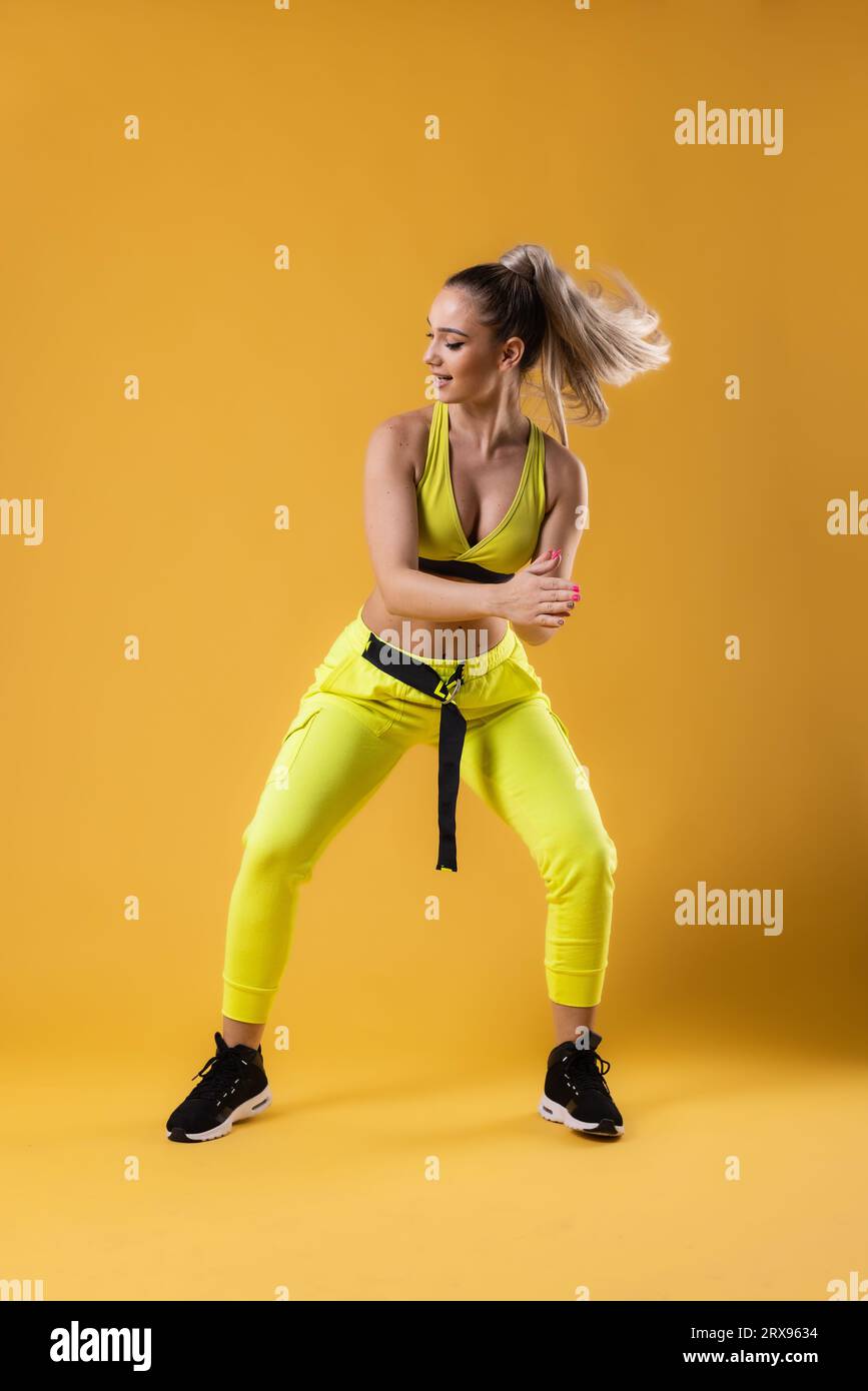 Beautiful girl in yellow outfit dancing zumba. Happy dance instructor against dark yellow or orange background. Stock Photo