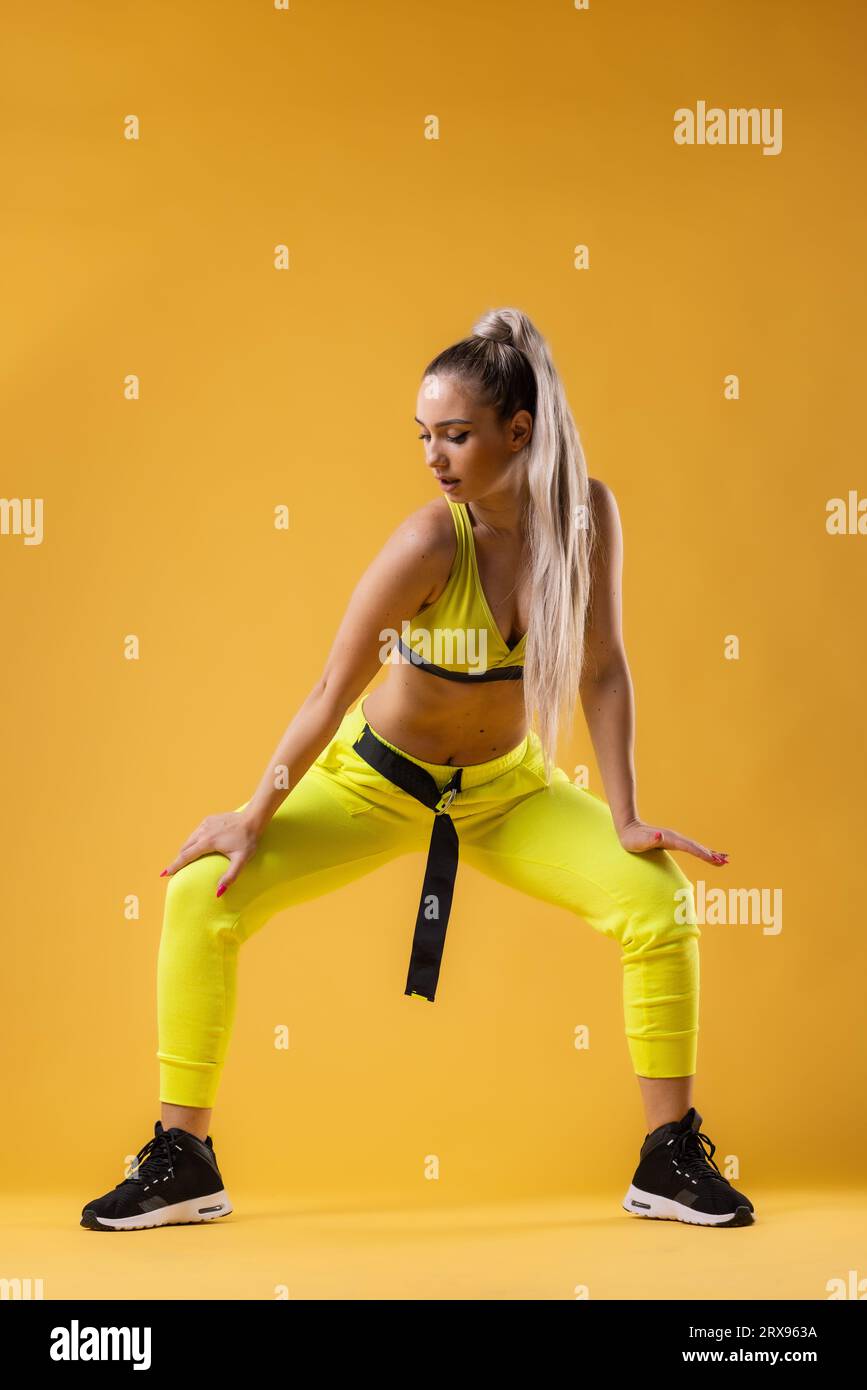 Beautiful girl in yellow outfit dancing zumba. Happy dance instructor against dark yellow or orange background. Stock Photo